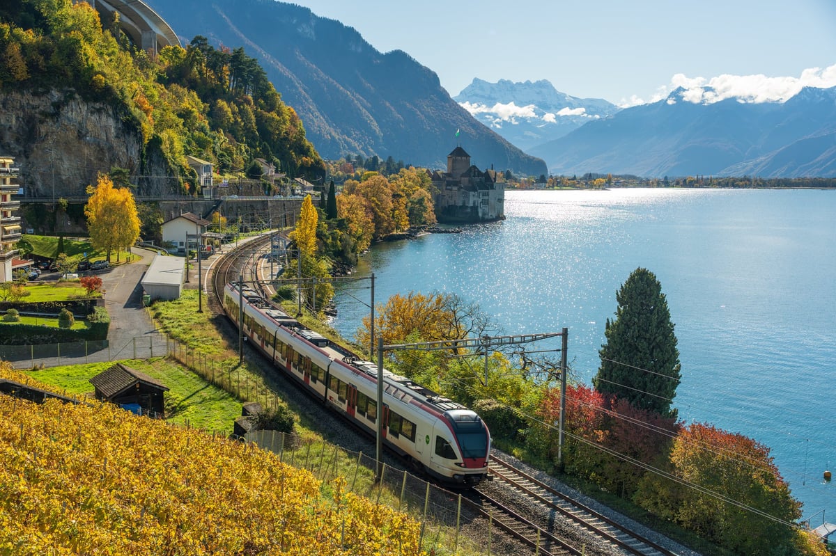Train passing a castle on a lake shore at sunrise